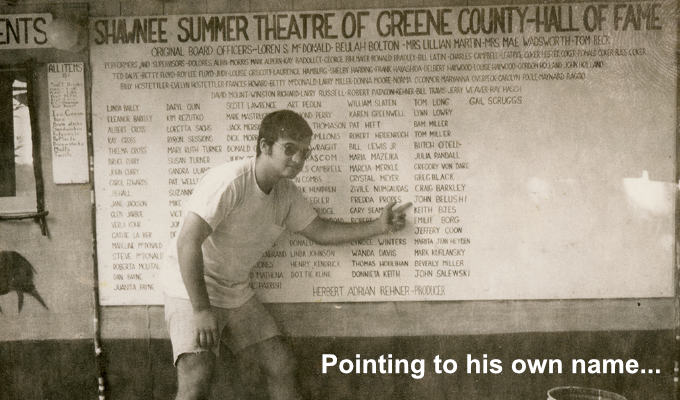 John Belushi pointing to his own name on a list of summer theatre alumni