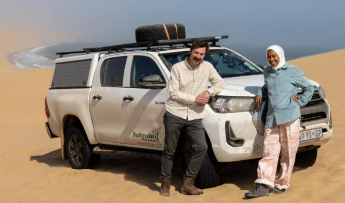 Mike and Ola leaning on their car on a sand dune