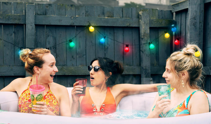 Three women drinking cocktails in a hottub in their back garden