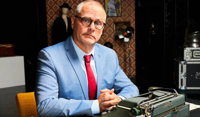 Dee in a pale blue suit sitting at a vintage typewriter for Hancock documentary