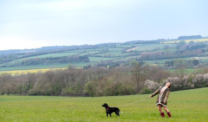 Picture shows Lucy, a tiny figure in a vast field, with a dog