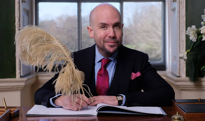 Tom signing a wedding register with a big plume pen