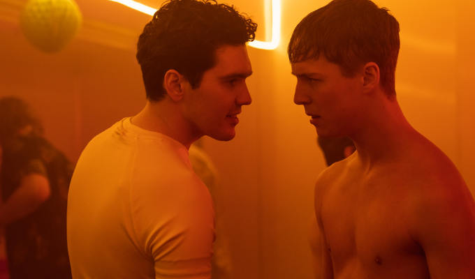 Two young men, one topless, looking longingly at each other at a party in Wrecked